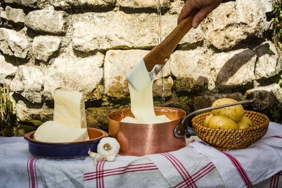 L'Aligot Fromage fondu servi dans un plat en cuivre avec des pommes de terre à côté.